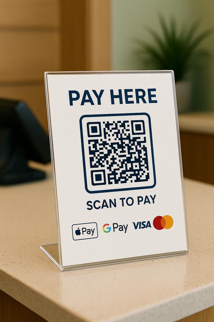 An acrylic pay-here QR code sign standing on a shop counter, listing Apple Pay, Google Pay, Visa and Mastercard